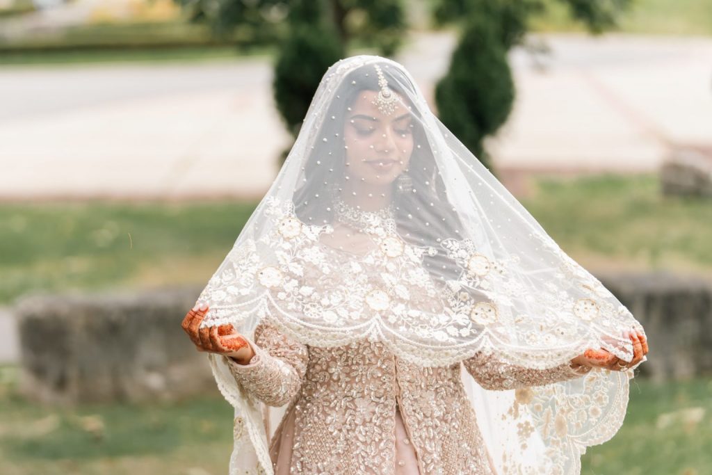 bride holding veil over face during outdoor wedding photoshoot