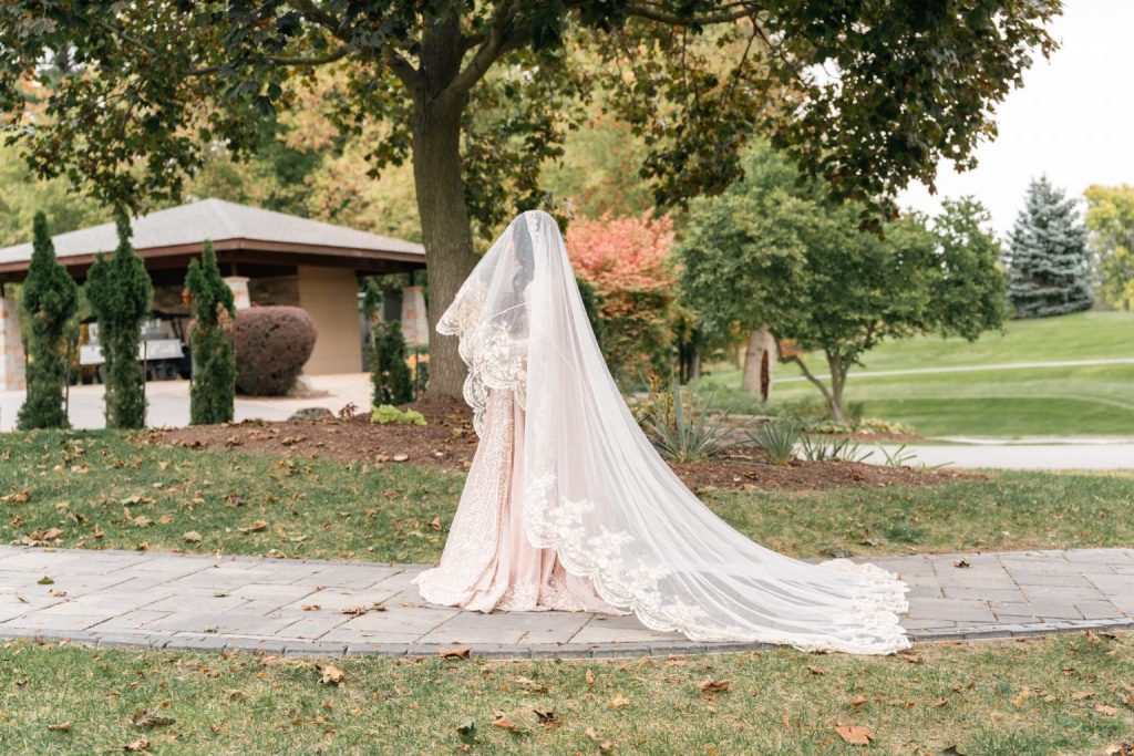 bride standing outdoors with long flowing wedding veil in garden